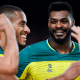 Lucarelli e Isac sorriem durante partida da Liga das Nações de vôlei masculino, a VNL. Eles ficaram fora do duelo contra a Polônia