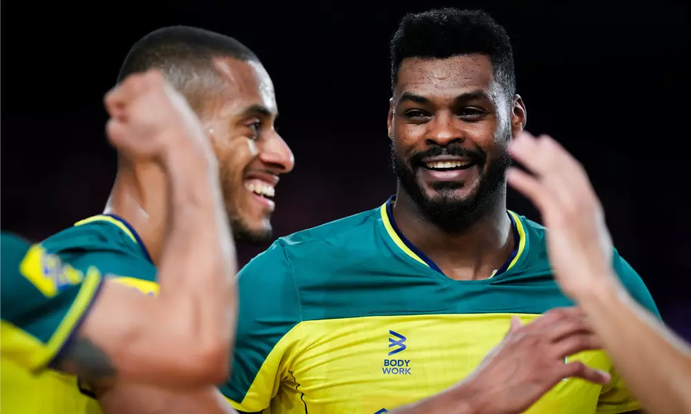 Lucarelli e Isac sorriem durante partida da Liga das Nações de vôlei masculino, a VNL. Eles ficaram fora do duelo contra a Polônia