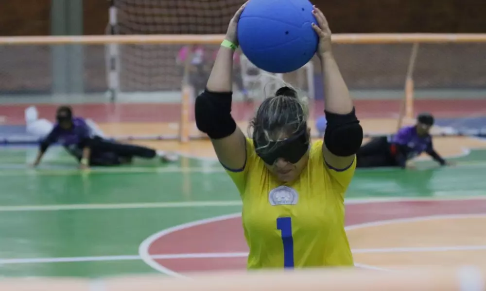 Foto tirada de trás do gol do Ierc mostra a ala Larissa Leite com a bola sobre a cabeça iniciando o movimento do arremesso por entre as pernas enquanto, ao fundo, aparecem atletas da ACSB desfocadas deitadas em posição defensiva em jogo do Regional Nordeste