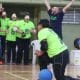 Jimena ergue o braço direito segurando a bola azul para tomar o impulso do arremesso. A foto foi tirada de trás do gol do Maestro.