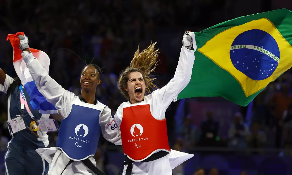 Carol Moura e atleta francesa com bandeira de seus países após a final do taekwondo em Paris-2024