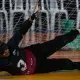 Vestindo uniforme preto com o número 3, venda preta e luvas sem dedos, Adria está deitada de lado em uma quadra coberta, bloqueando a bola azul que rola nas proximidades. Atrás dela, há uma rede. O fundo mostra cadeiras brancas e alguns objetos verdes atrás da rede. A linguagem corporal da atleta indica foco e esforço enquanto ela estica os braços e as pernas. Foto: Itamar Aguiar/ CBDV