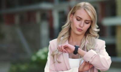 Pessoa olhando o relógio ou celular, em ambiente de trabalho ou casa, com expressão de indecisão sobre treinar.