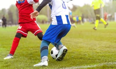 Jogador mudando rapidamente de direção ou disputando bola em equilíbrio instável, com foco no apoio dos pés e controle corporal.