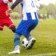 Jogador mudando rapidamente de direção ou disputando bola em equilíbrio instável, com foco no apoio dos pés e controle corporal.