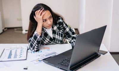 Pessoa sentada com expressão de esgotamento mental, cercada por trabalho e estímulos digitais.