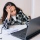 Pessoa sentada com expressão de esgotamento mental, cercada por trabalho e estímulos digitais.
