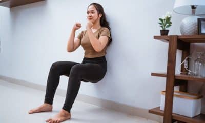 Pessoa fazendo prancha ou cadeira na parede em casa, com postura alinhada e ambiente claro.