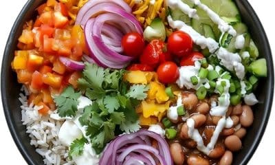 Prato colorido com arroz, feijão, salada, legumes e ervas naturais, ao lado de temperos como alho, limão e manjericão.
