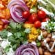Prato colorido com arroz, feijão, salada, legumes e ervas naturais, ao lado de temperos como alho, limão e manjericão.