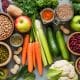 Prato com frutas, aveia, sementes, legumes e copo de água ao lado, em ambiente claro e natural.